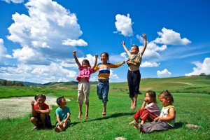 group of children playing in a green lawn with a bright blue sky and fluffy white clouds behind them