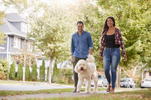 Couple Walking Dog Along Suburban Street