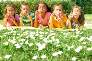 Portrait of cute friends having bubble fun on green lawn in park