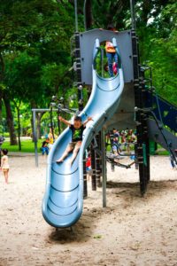 Chil on slide in playground with trees in background