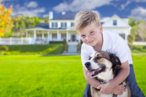 Happy Young Boy and His Dog in Front Yard of Their House.